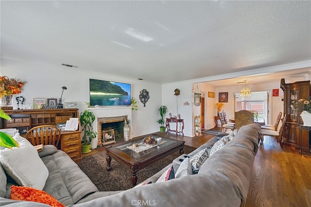 living room featuring a fireplace, a notable chandelier, visible vents, a textured ceiling, and wood finished floors