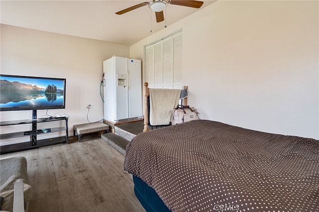 bedroom featuring white refrigerator with ice dispenser, a ceiling fan, and wood finished floors