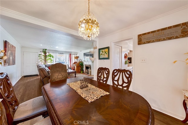 dining space featuring a fireplace, ornamental molding, a chandelier, and wood finished floors