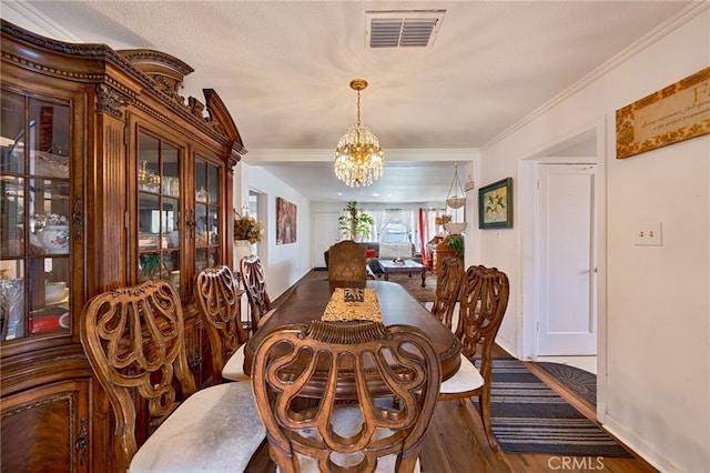 dining area featuring crown molding, visible vents, a notable chandelier, and wood finished floors