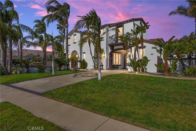 view of front of property with a balcony, a lawn, and stucco siding