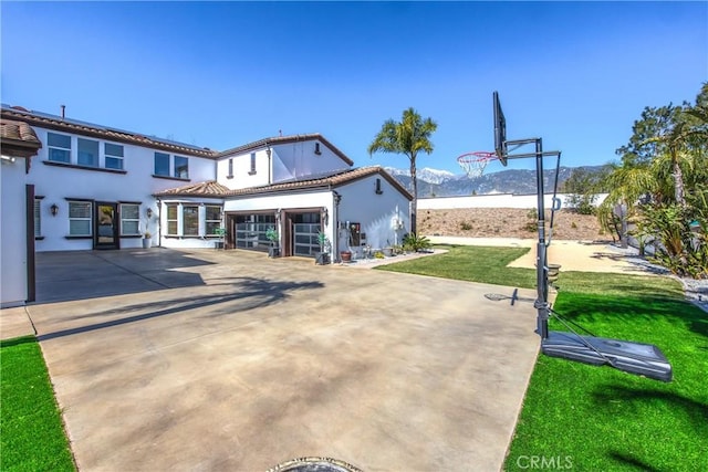 rear view of property featuring stucco siding, concrete driveway, a lawn, a mountain view, and a garage