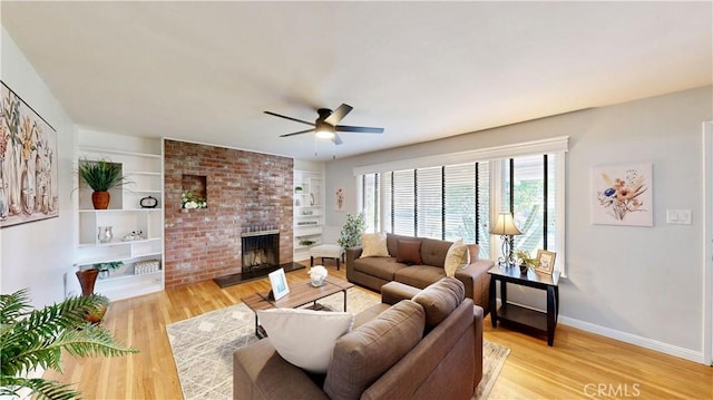 living area featuring light wood finished floors, a brick fireplace, built in shelves, and baseboards