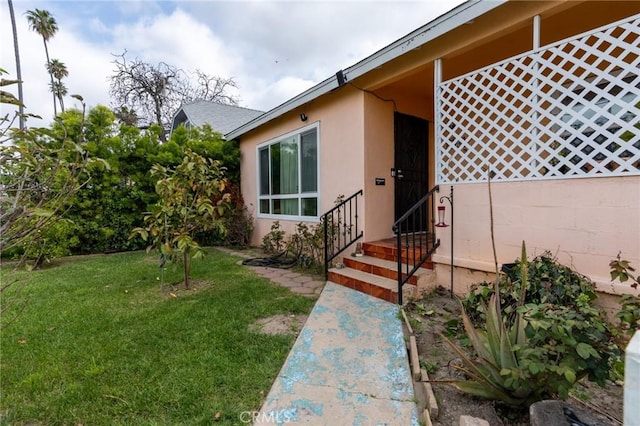 view of exterior entry with stucco siding and a yard