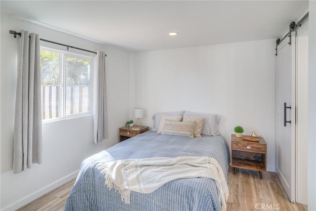 bedroom featuring light wood-style floors, recessed lighting, baseboards, and a barn door