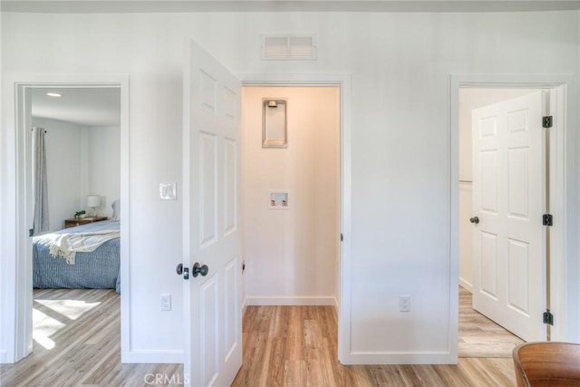 hall with light wood-type flooring, visible vents, and baseboards