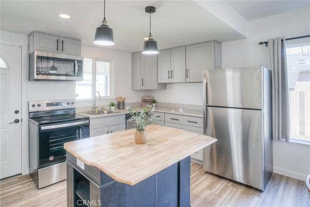 kitchen with gray cabinetry, stainless steel appliances, a sink, light countertops, and a center island