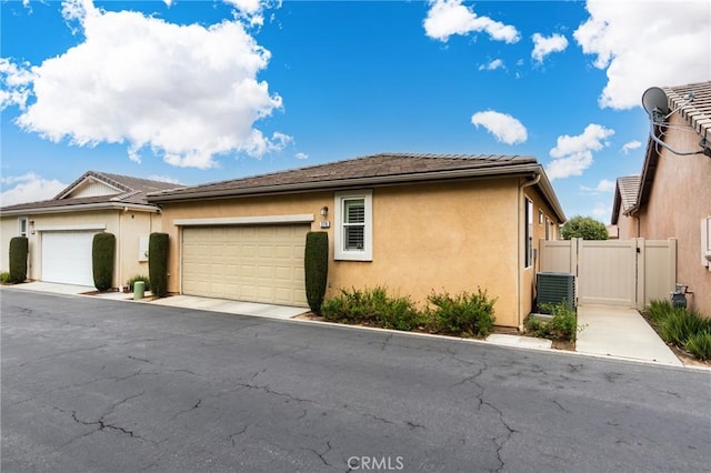 view of side of property with stucco siding, an attached garage, a gate, fence, and a tiled roof