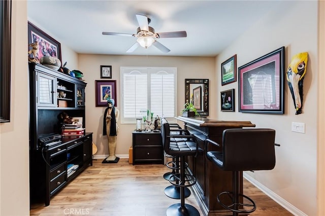 office area with a bar, light wood finished floors, baseboards, and a ceiling fan