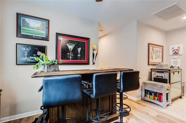 bar featuring a dry bar, baseboards, visible vents, and wood finished floors