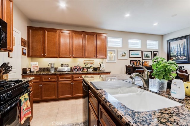 kitchen featuring brown cabinets, light tile patterned floors, a sink, dark stone counters, and black appliances