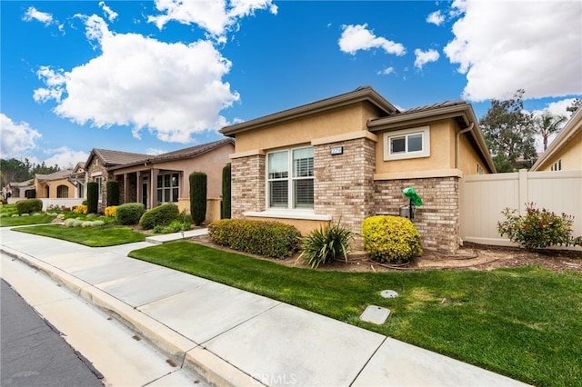 view of front of property with brick siding, a front yard, fence, and stucco siding