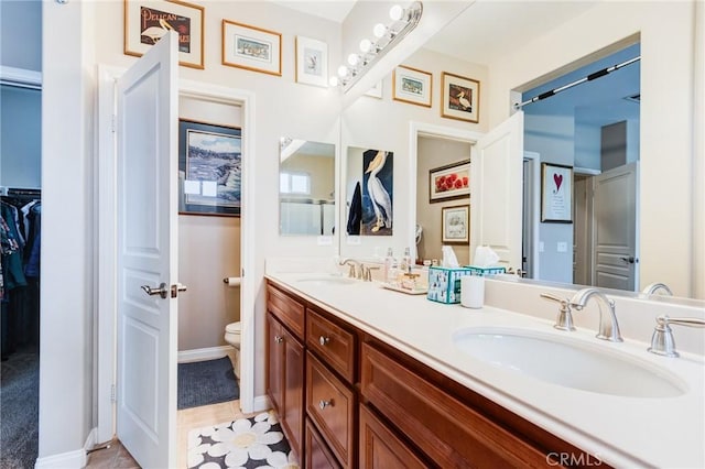 bathroom featuring toilet, double vanity, a walk in closet, and a sink