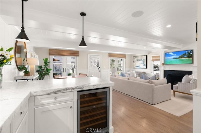 kitchen with light stone countertops, wine cooler, pendant lighting, and white cabinets