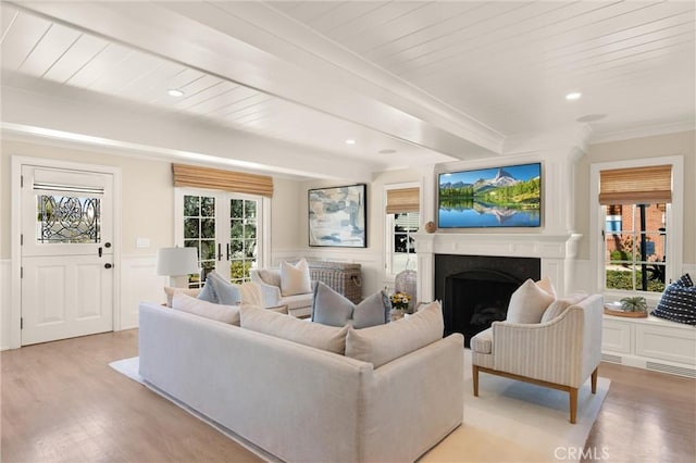 living room with light wood finished floors, a wainscoted wall, beamed ceiling, a fireplace, and a decorative wall