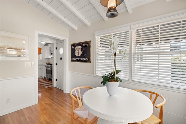 dining area with lofted ceiling with beams, light wood-style floors, a wealth of natural light, and a ceiling fan