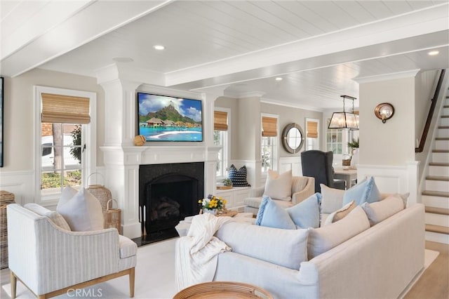 living room featuring a fireplace with flush hearth, a wainscoted wall, crown molding, and stairway