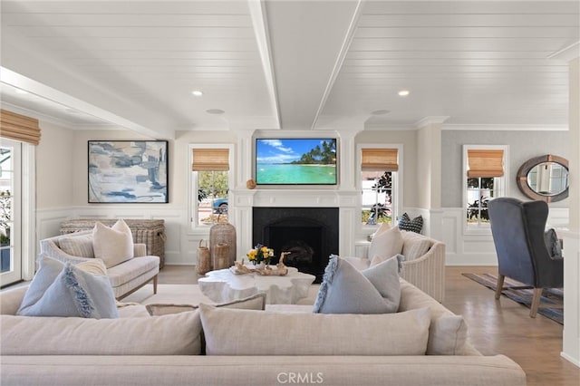 living room with light wood-type flooring, a high end fireplace, a wainscoted wall, and beamed ceiling