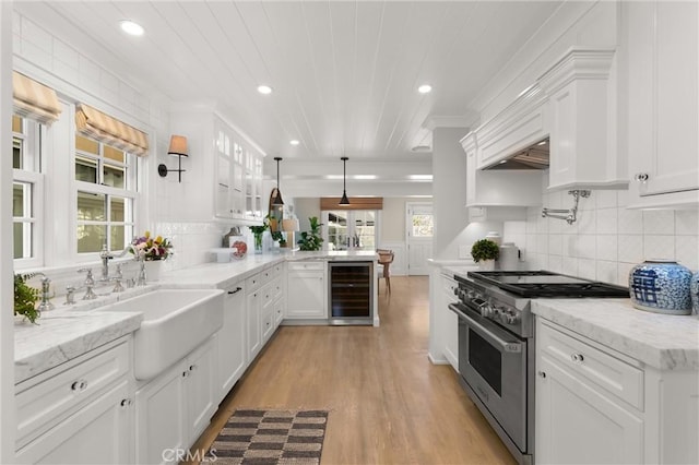 kitchen featuring wine cooler, hanging light fixtures, high end stainless steel range oven, white cabinetry, and a sink