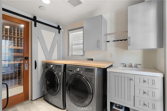 washroom featuring washing machine and clothes dryer, cabinet space, visible vents, a barn door, and a sink