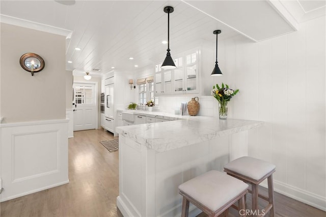 kitchen with a peninsula, white cabinets, hanging light fixtures, a kitchen bar, and glass insert cabinets