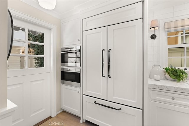 kitchen featuring paneled refrigerator, stainless steel double oven, light stone countertops, and white cabinets