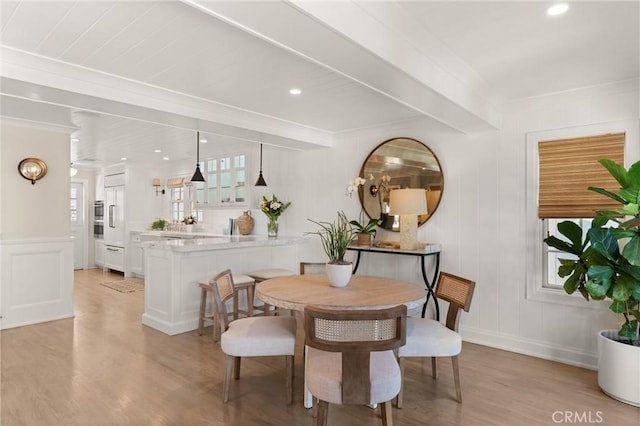 dining space with beamed ceiling, recessed lighting, light wood-style flooring, and a decorative wall