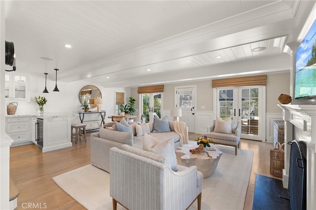 living area featuring light wood-type flooring, french doors, wainscoting, and beverage cooler