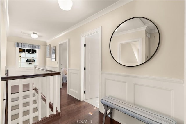 hallway with a decorative wall, ornamental molding, dark wood-type flooring, wainscoting, and an upstairs landing