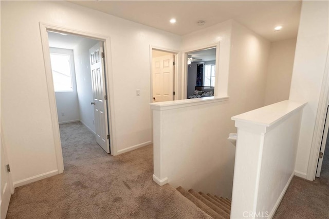 corridor with baseboards, light colored carpet, and an upstairs landing