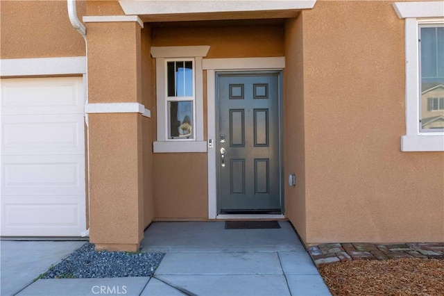 entrance to property featuring a garage and stucco siding