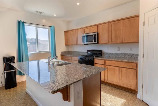 kitchen with black gas range, a kitchen island with sink, a sink, visible vents, and stainless steel microwave