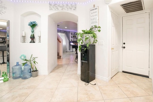 corridor featuring light tile patterned floors, baseboards, visible vents, arched walkways, and stairs