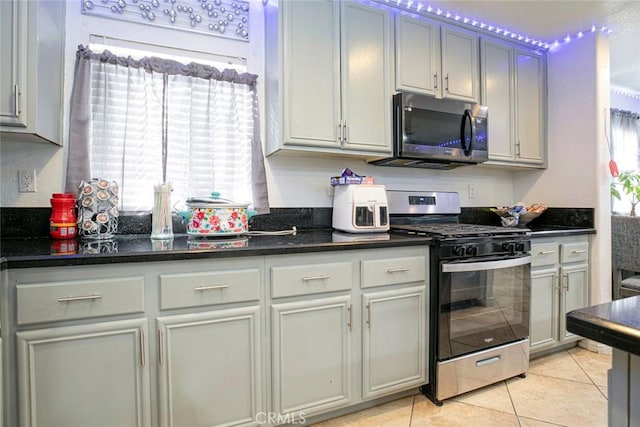 kitchen featuring a healthy amount of sunlight, light tile patterned floors, appliances with stainless steel finishes, and dark stone countertops