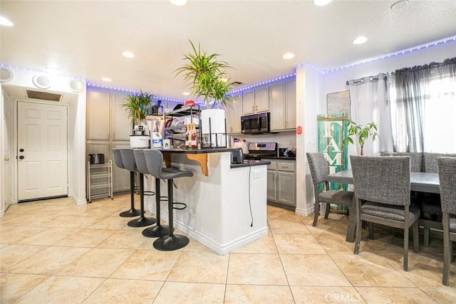 kitchen featuring light tile patterned floors, visible vents, stainless steel electric stove, dark countertops, and a kitchen bar