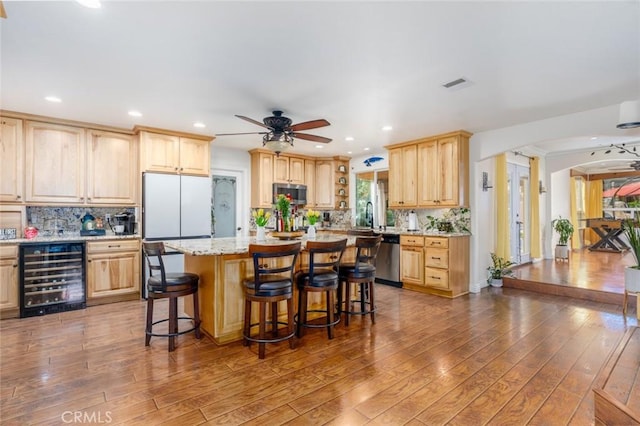 kitchen with wine cooler, appliances with stainless steel finishes, a breakfast bar, light stone countertops, and light brown cabinets