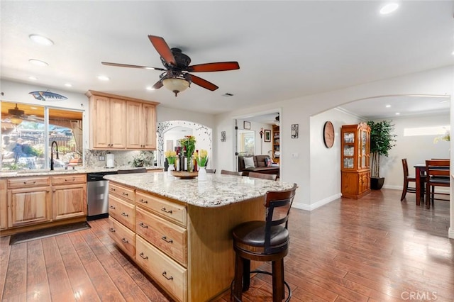 kitchen featuring arched walkways, dishwasher, a kitchen island, dark wood-type flooring, and light brown cabinets