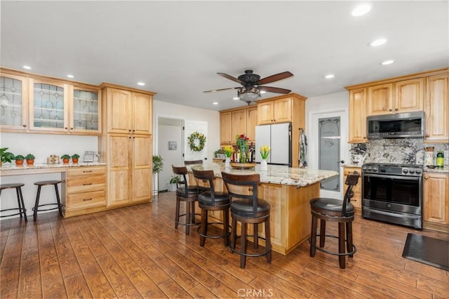 kitchen featuring a center island, stainless steel appliances, glass insert cabinets, light stone countertops, and a kitchen breakfast bar