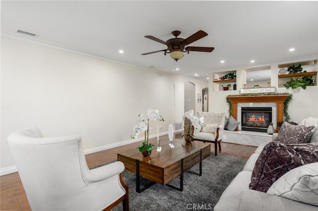 living area with arched walkways, visible vents, crown molding, and wood finished floors