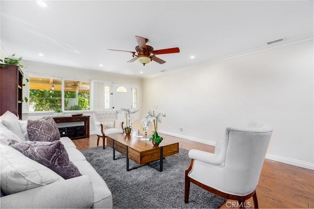 living room featuring ornamental molding, visible vents, baseboards, and wood finished floors