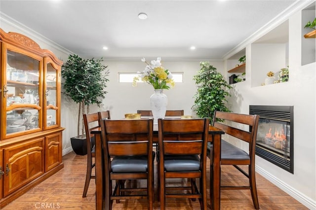 dining area with recessed lighting, light wood-style flooring, ornamental molding, and a glass covered fireplace