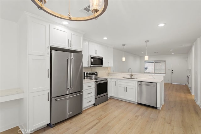 kitchen featuring light wood-style flooring, appliances with stainless steel finishes, white cabinetry, a sink, and a peninsula