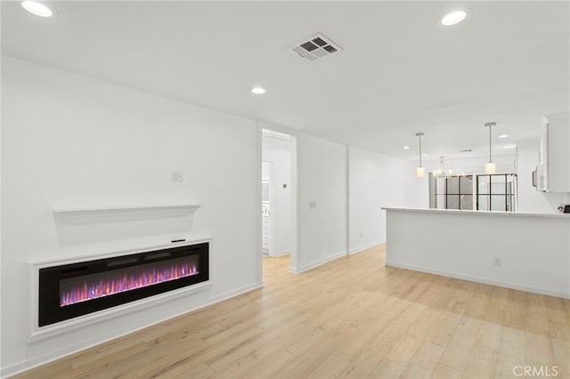 unfurnished living room with recessed lighting, visible vents, light wood-style floors, a glass covered fireplace, and baseboards