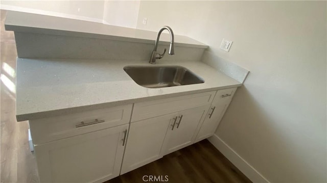 kitchen featuring baseboards, dark wood-style flooring, a sink, and white cabinets