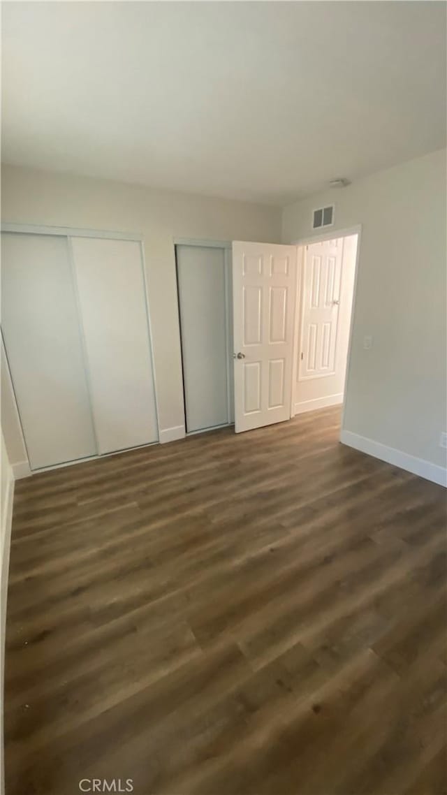 unfurnished bedroom with dark wood-style floors, two closets, visible vents, and baseboards