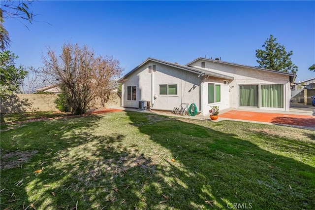 rear view of house with stucco siding, a lawn, a patio area, central AC, and fence