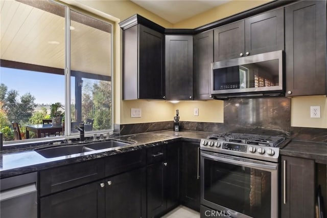 kitchen with stainless steel appliances, a sink, backsplash, and dark stone countertops