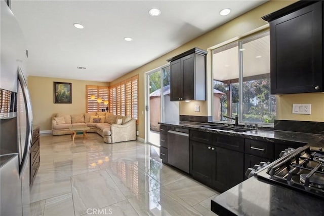 kitchen featuring stainless steel appliances, recessed lighting, open floor plan, a sink, and dark cabinets