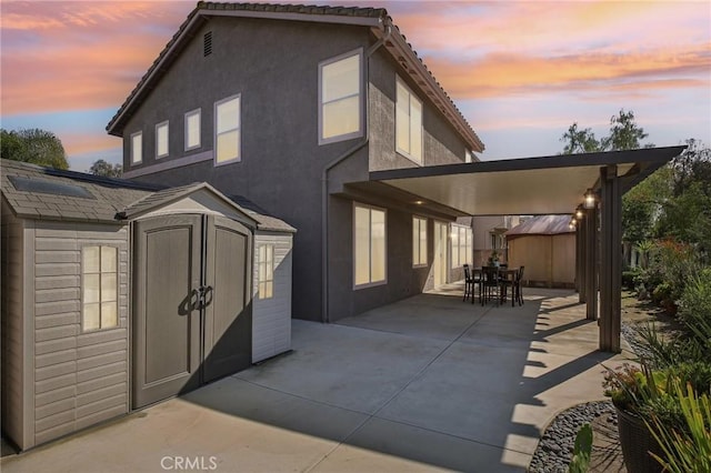 back of house with a shed, an outdoor structure, outdoor dining space, and stucco siding