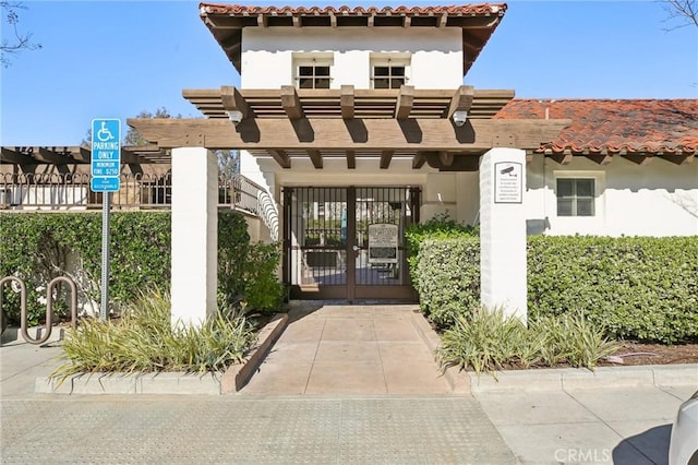 exterior space featuring a tiled roof, stucco siding, a gate, and a pergola